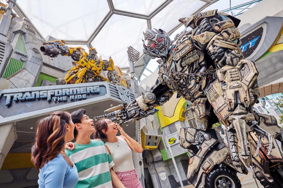 นักท่องเที่ยวถ่ายภาพกับหุ่นยนต์ทรานส์ฟอร์เมอร์หน้าเครื่องเล่น Transformers The Ride ที่ Universal Studios Singapore